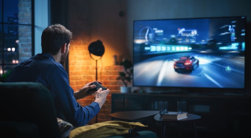 A person is shown playing a racing game on his television at home.
