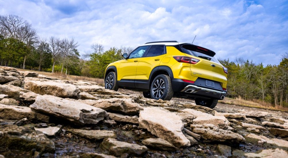 A yellow 2024 Chevy Trailblazer Activ is shown from the rear parked on rocks after visiting a Chevy dealer in the city.
