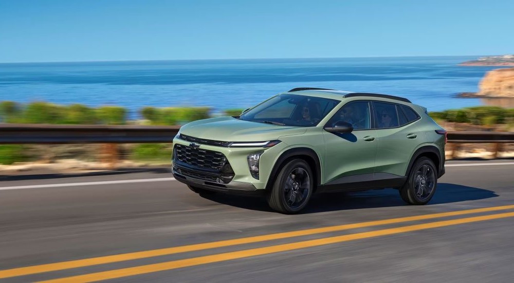 A light green 2024 Chevy Trax is shown driving past an ocean.