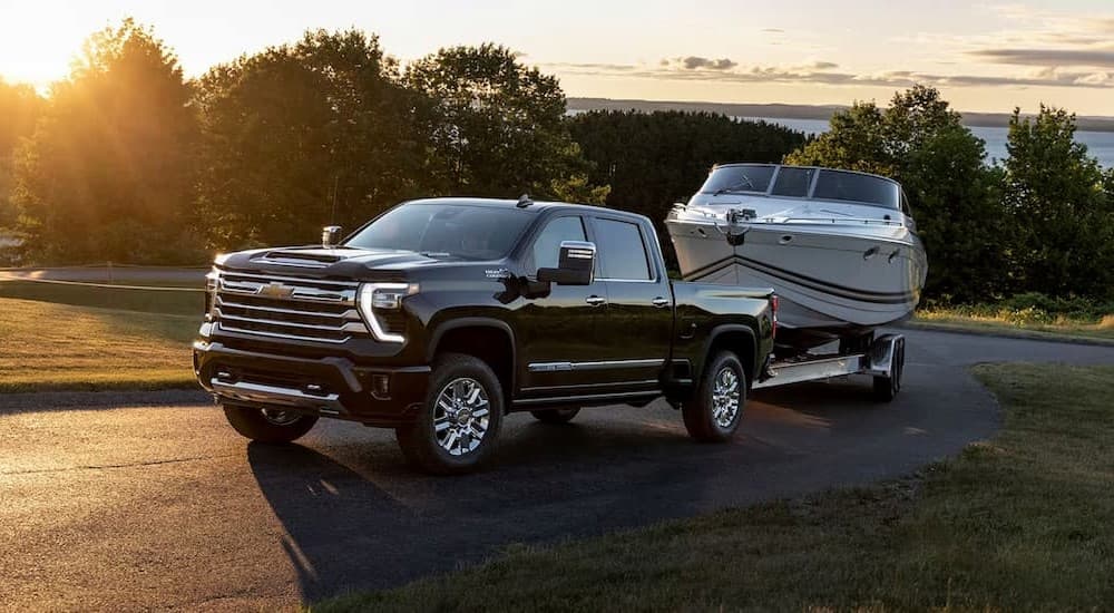 A black 2024 Chevy Silverado 3500HD High Country is shown towing a boat.