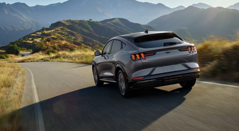 A grey 2023 Ford Mustang Mach-E is shown driving on a mountain road.