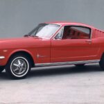 A red 1965 Ford Mustang is shown parked near a Ford dealer.
