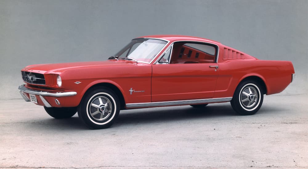 A red 1965 Ford Mustang is shown parked near a Ford dealer.