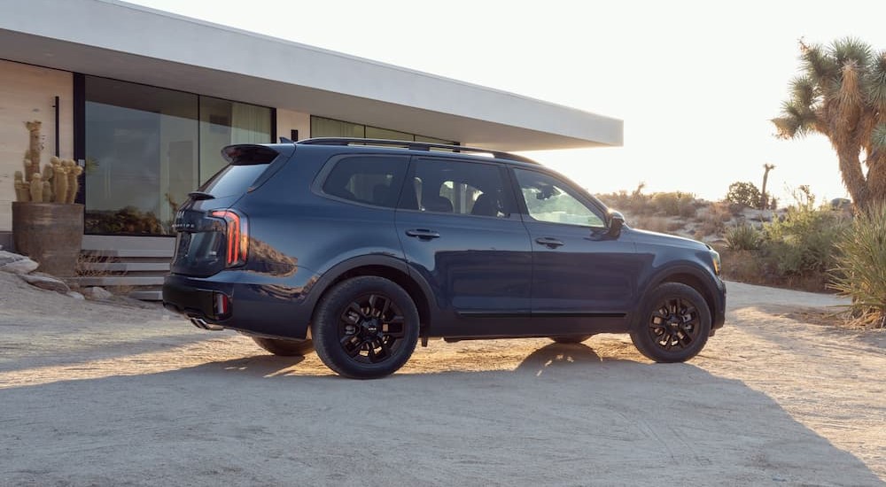 A blue 2024 Kia Telluride is shown parked near a house.