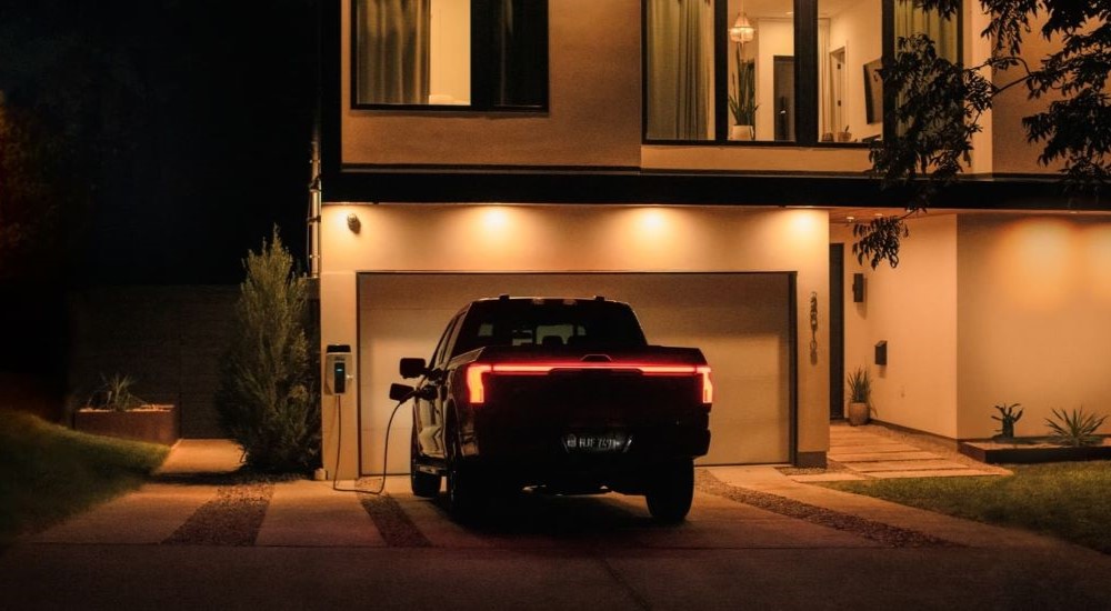 A black 2022 Ford F-150 Lightning is shown charging in front of a garage after looking a used EVs for sale near you.