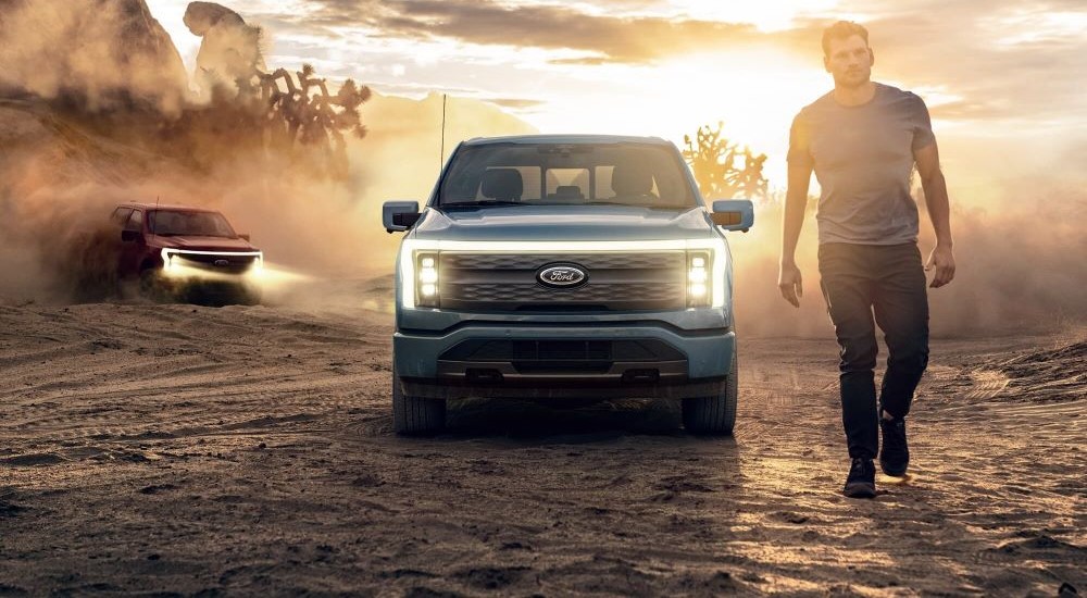 A red and a blue 2022 Ford F-150 Lightning are shown on a sunny day.