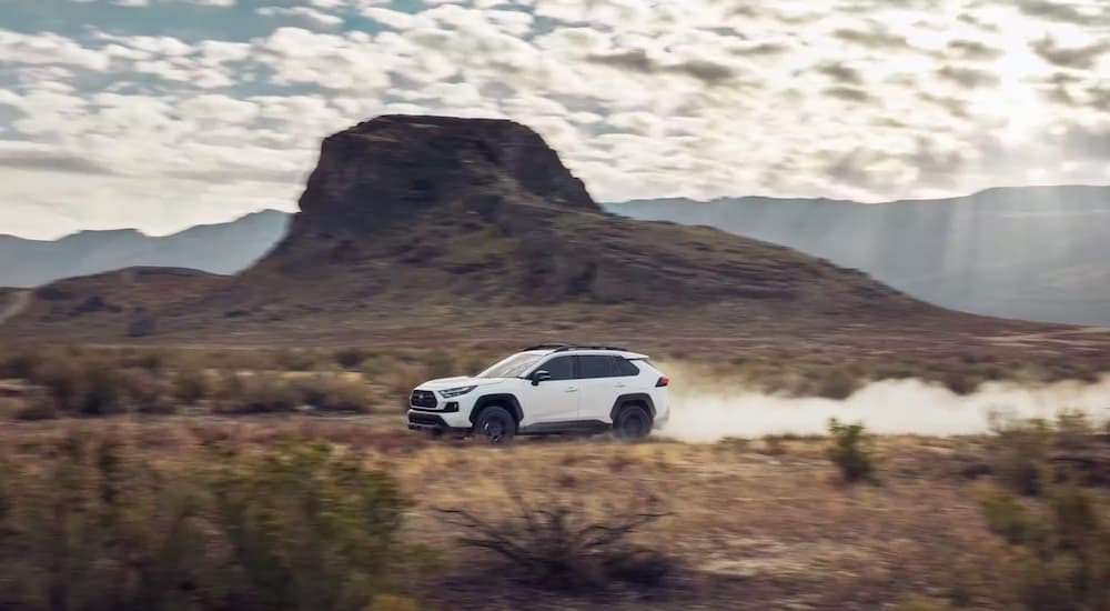 A white 2023 Toyota RAV4 TRD is shown from the side while off-road after leaving a Toyota dealer.