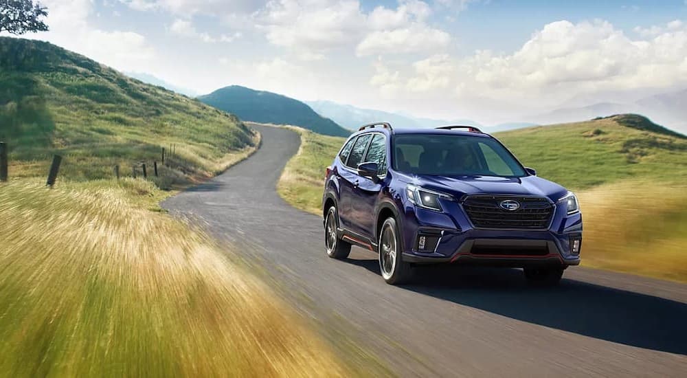 A blue 2023 Subaru Forester is shown driving on a winding road.