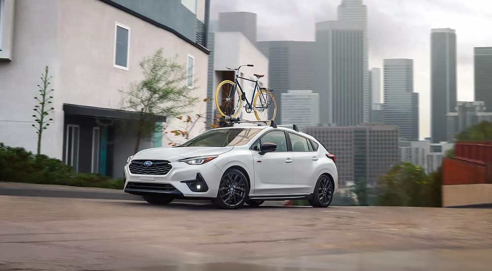 A white 2024 Subaru Impreza RS is shown driving near a city.