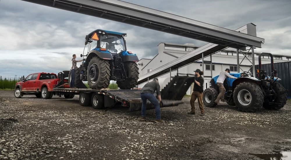 A red 2023 Ford Super Duty F-450 is shown towing a trailer near a farm.