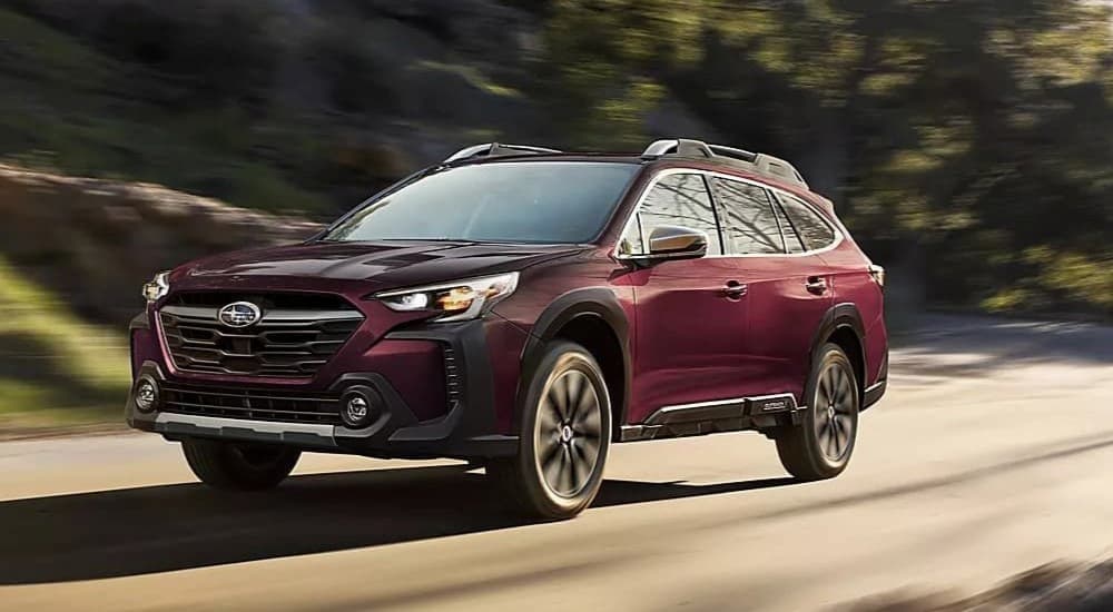 A purple 2023 Subaru Outback is shown driving on a road after visiting a used car dealer.