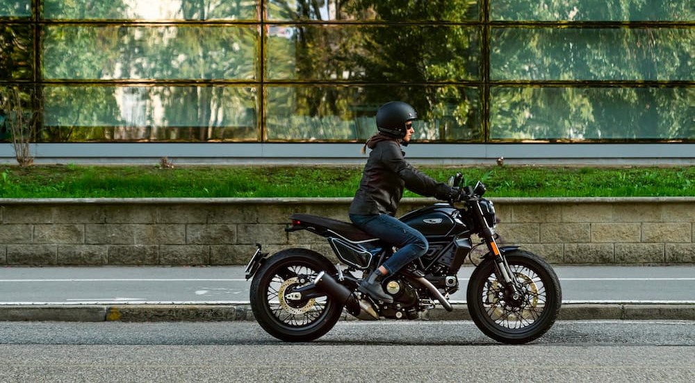 A person is shown riding a black 2023 Ducati Scrambler after viewing used motorcycles for sale.