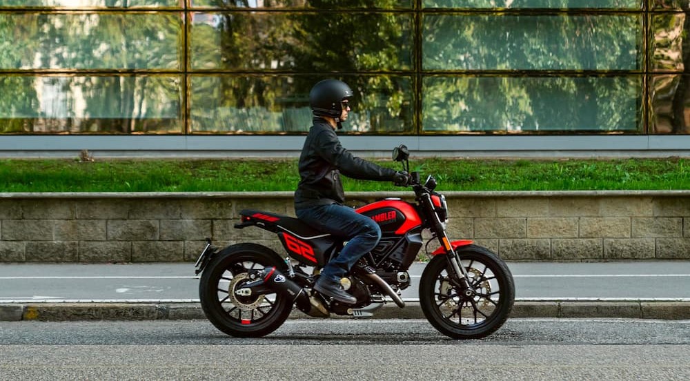 A black and red 2023 Ducati Scrambler is shown being driven on a street.