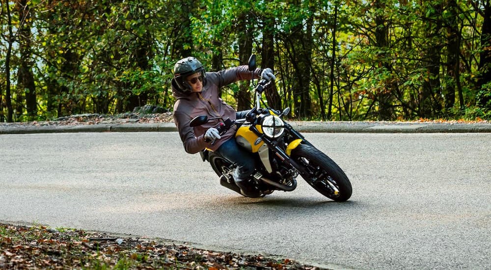 A yellow 2023 Ducati Scrambler is shown driving on a road.