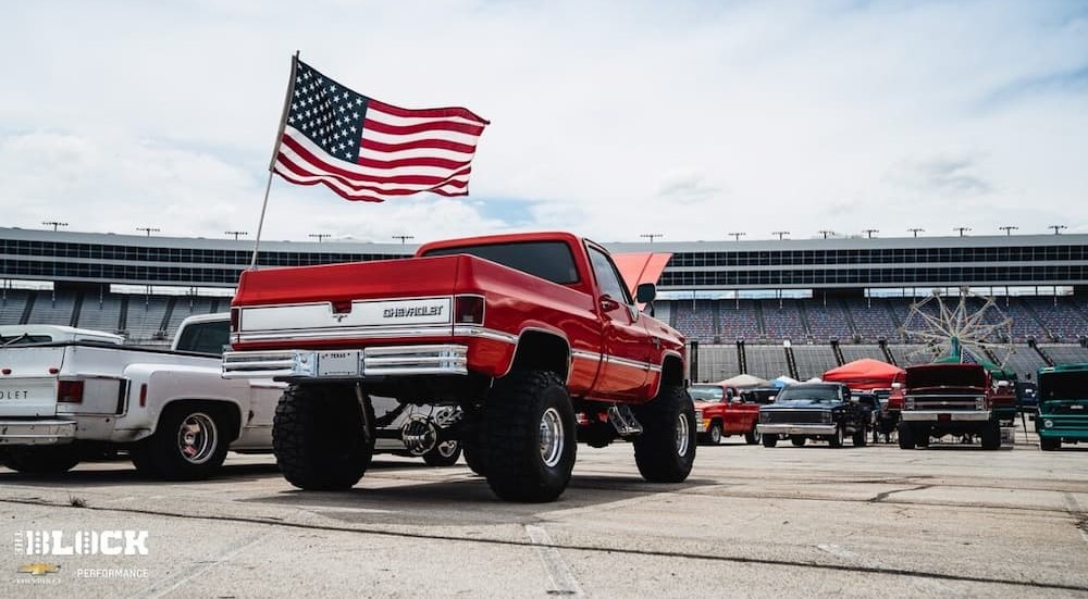 A red 1987 Chevrolet K10 Pickup is shown parked near a used Chevy dealership.