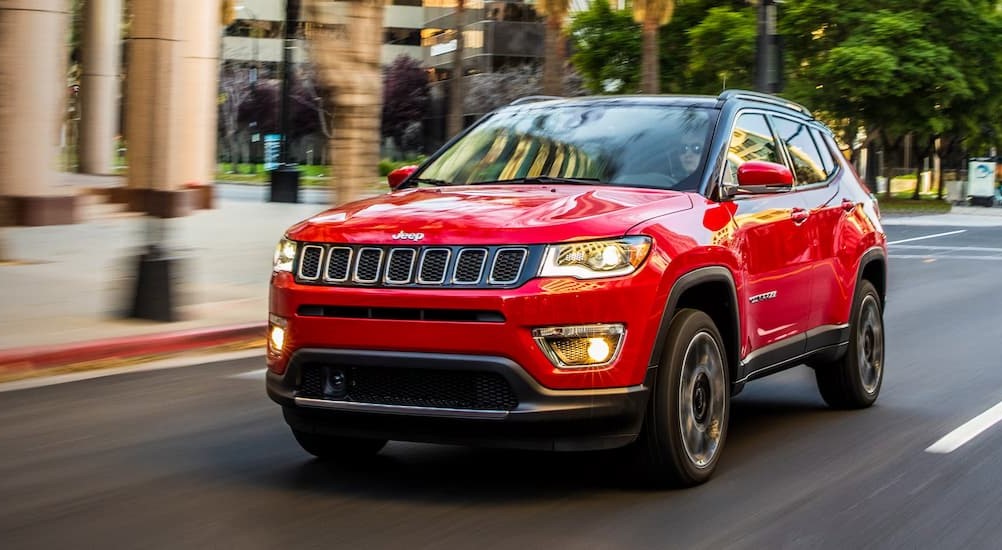 A red 2018 Jeep Compass is shown driving on a city street after performing a headlight replacement.