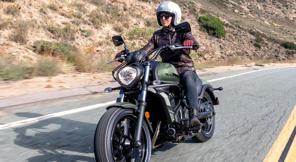 A woman is shown driving a 2022 Kawasaki Vulcan S on a desert road.