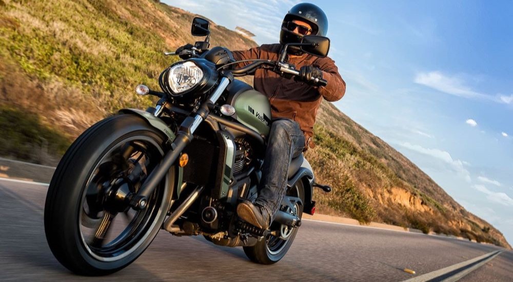 A man is shown driving a black 2022 Kawasaki Vulcan S down a desert road after visiting a Kawasaki motorcycle dealer.