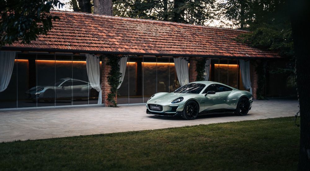 A teal 2026 Caterham Project V is shown from afar parked next to a building.