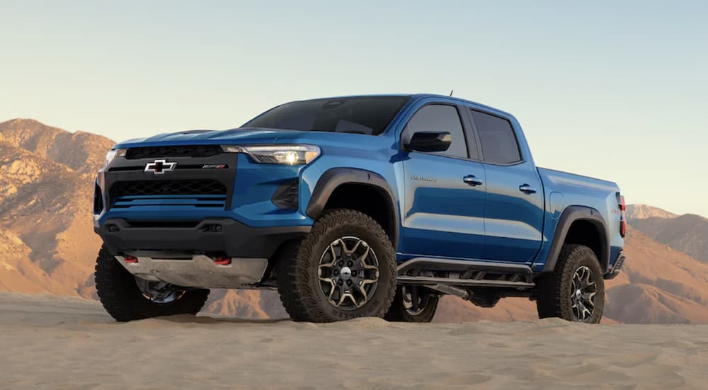 A blue 2023 Chevy Colorado ZR2 is shown driving up a desert road.