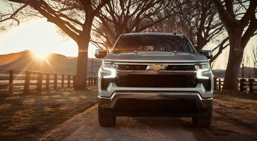 A grey 2023 Chevy Silverado 1500 LT is shown driving on a countryside road.