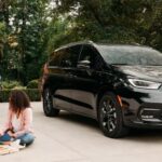 A black 2023 Chrysler Pacifica for sale is shown parked on a driveway near a family.