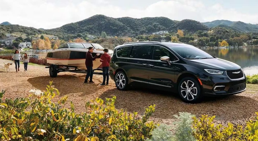 A black 2023 Chrysler Pacifica is shown towing a boat.