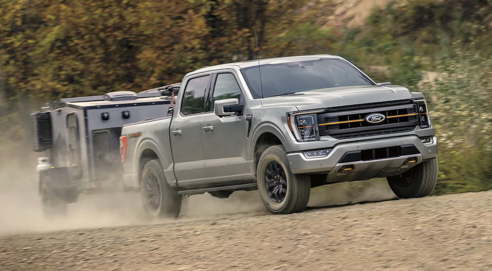 A grey 2023 Ford F-150 Tremor is shown towing a small camping trailer on a dusty dirt road.