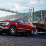 A red 2023 Ford F-150 XLT is shown towing a boat out of a body of water.