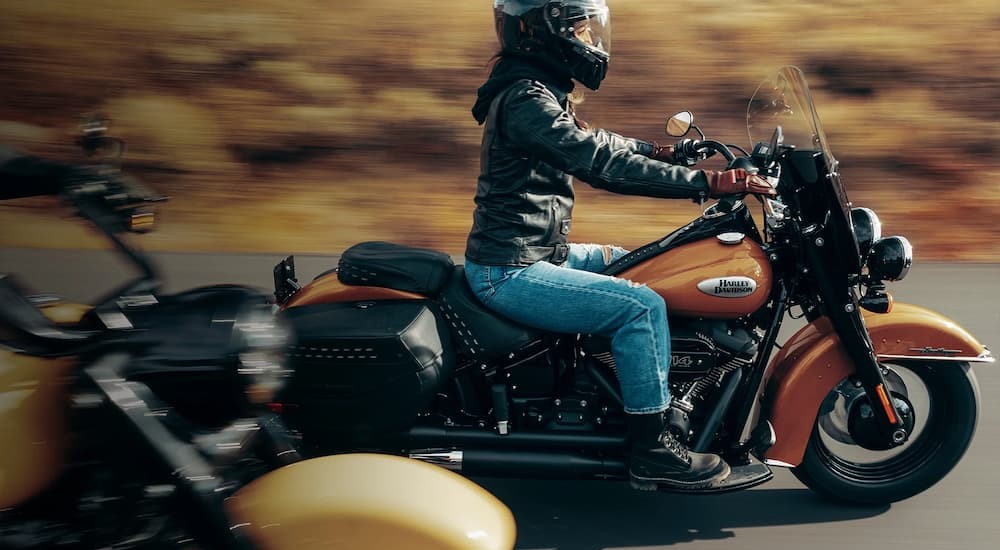 A person is shown riding a black and orange 2023 Harley-Davidson Heritage Classic on a highway after visiting a Harley-Davidson store..
