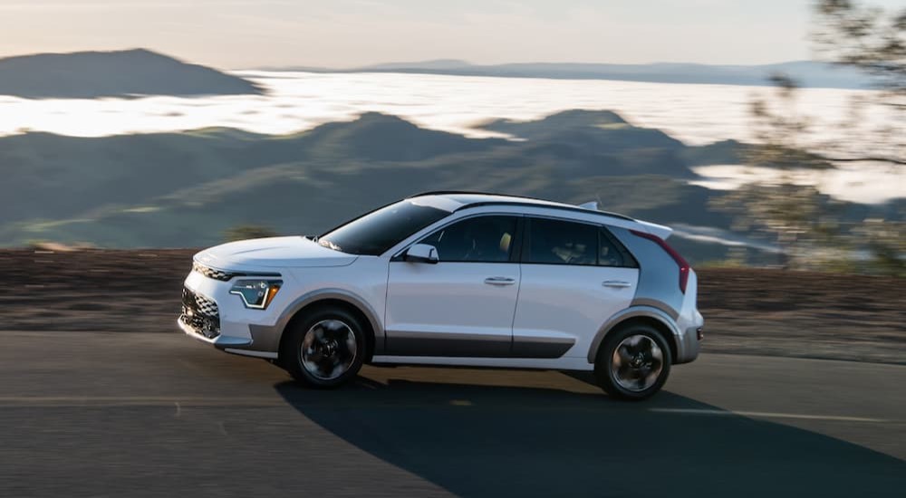 A white 2023 Kia Niro EV is shown driving on a road after viewing a Kia Niro for sale.