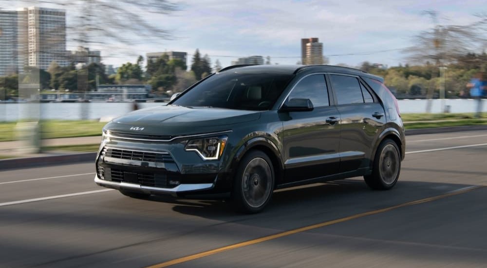 A green 2023 Kia Niro Hybrid is shown driving on a road near a city.