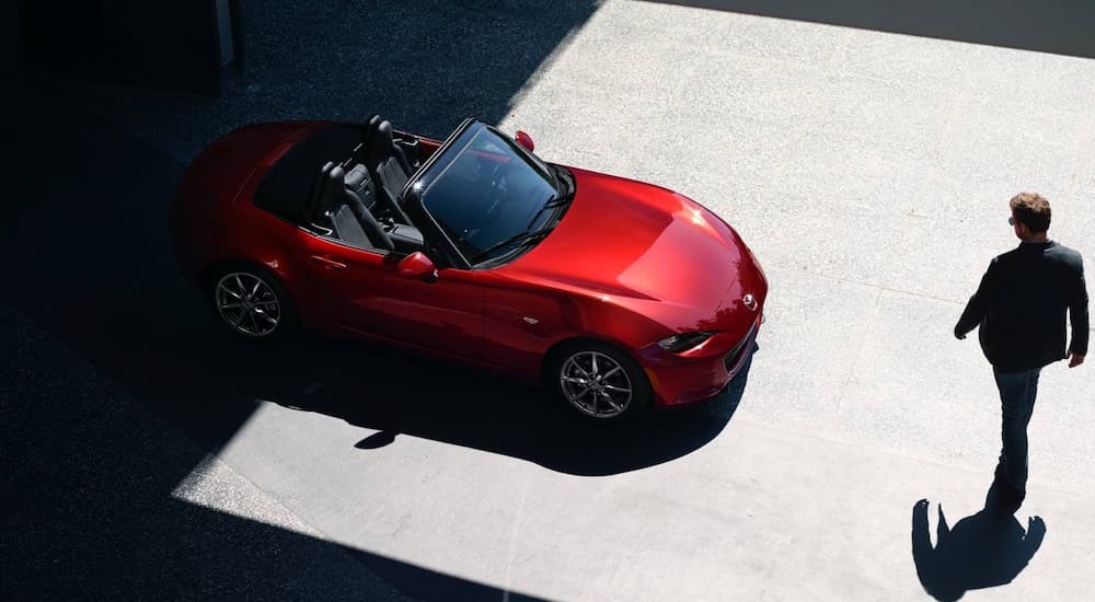 A red 2023 Mazda MX-5 Miata Roadster is shown from an aerial view near a person.