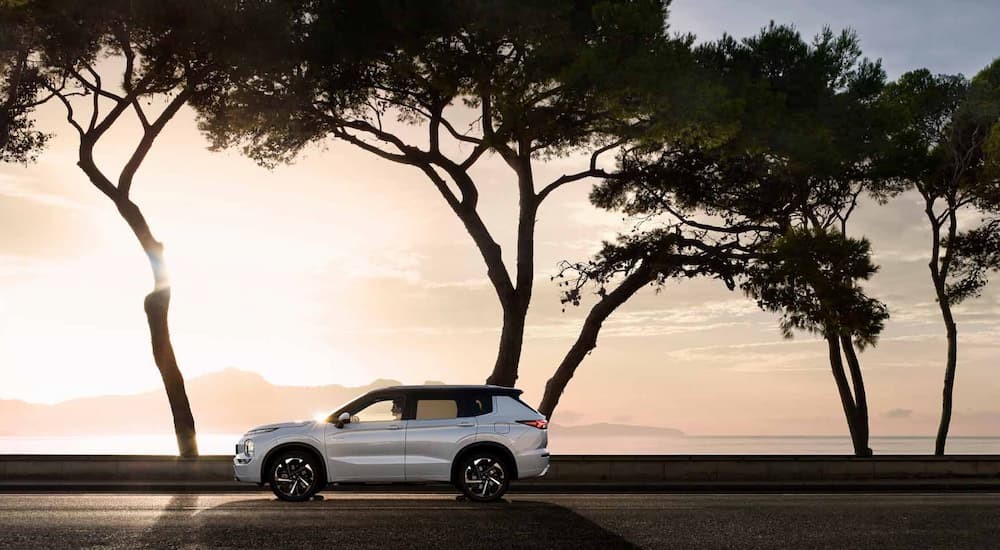 One of many popular electric vehicles for sale, a white 2023 Mitsubishi Outlander PHEV, is shown driving on a sunny day.