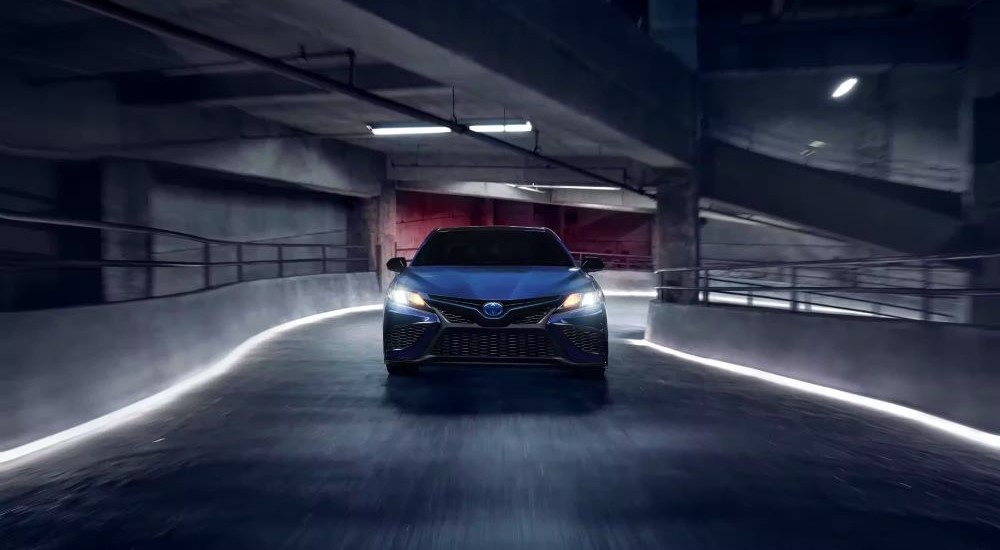A dark blue 2023 Toyota Camry Nightshade Edition is shown driving away from a Toyota dealer.