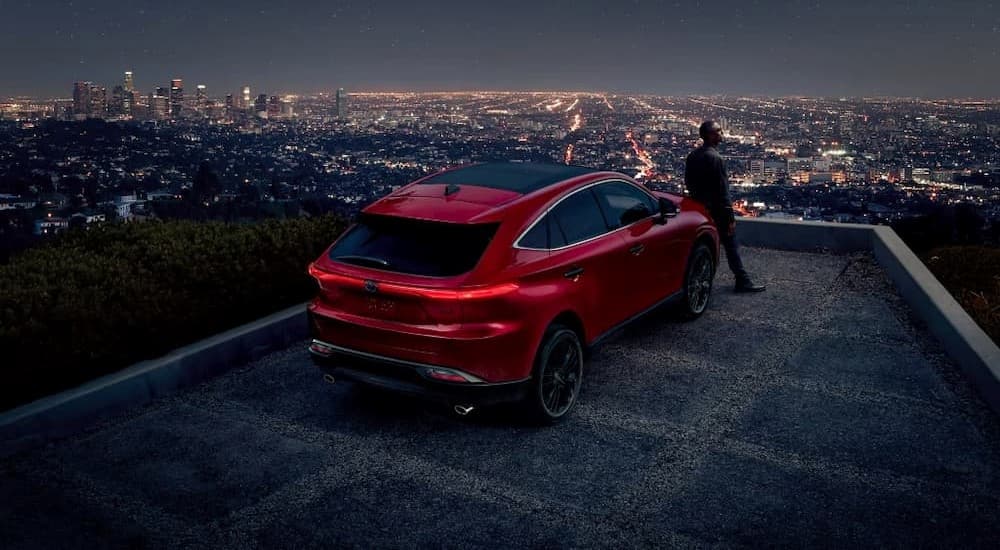 A person is shown leaning against the hood of a parked red 2023 Toyota Venza.