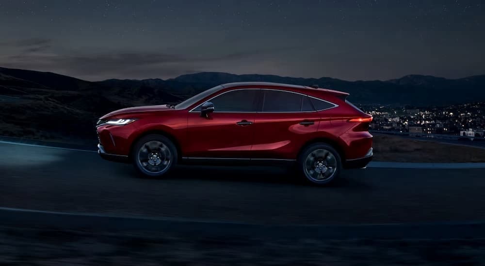 A red 2023 Toyota Venza is shown driving on a hill near a town.