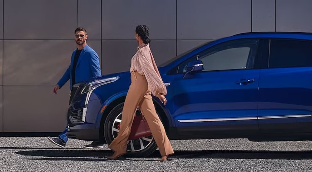 A blue 2024 Cadillac XT5 is shown parked near people walking.