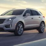 A white 2024 Cadillac XT5 for sale is shown to be driving on a road.