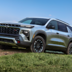 The newest Chevy Traverse for sale, a grey 2024 Chevy Traverse, is shown driving up a hill.