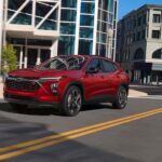 A red 2024 Chevy Trax RS is shown driving on a city road.