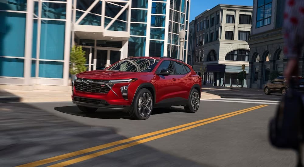 A red 2024 Chevy Trax RS is shown driving on a city road.