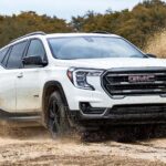 A white 2024 GMC Terrain AT4 is shown driving on a desert road.