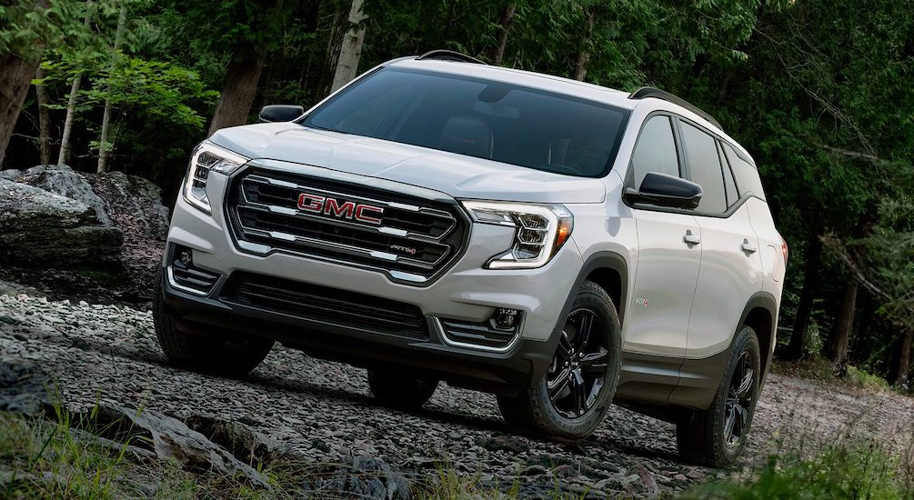 A white 2024 GMC Terrain AT4 is shown driving through a forest.