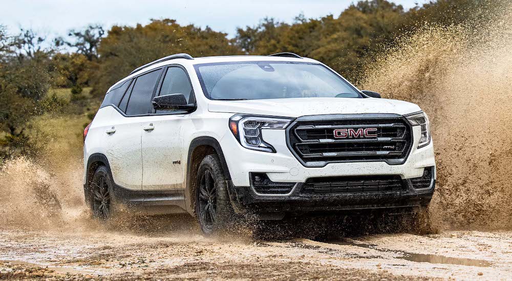 A white 2024 GMC Terrain AT4 is shown driving on a desert road.