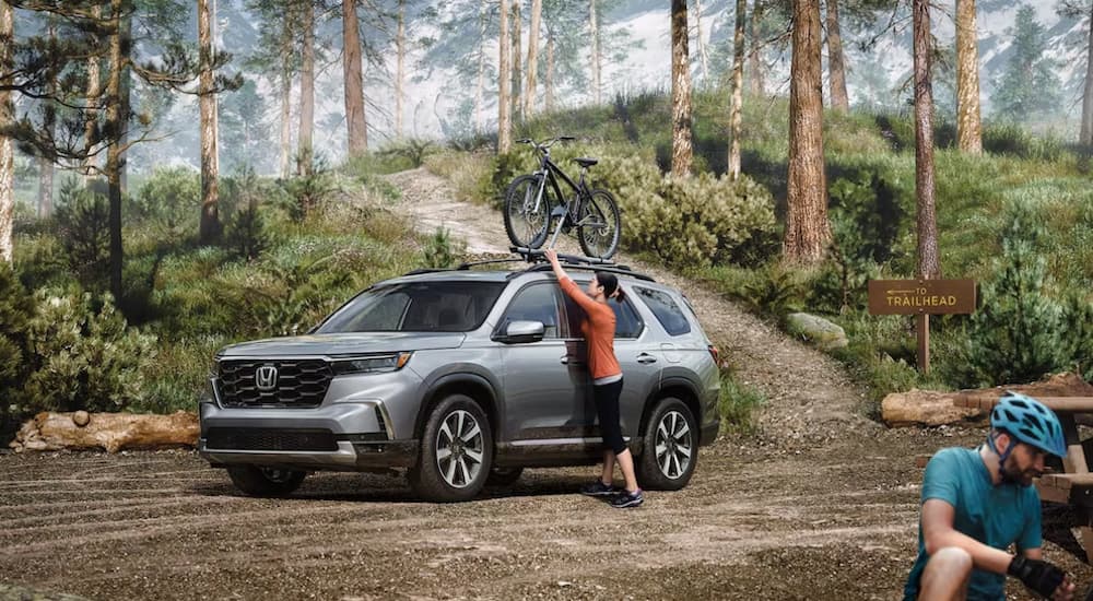 A person is shown loading a bicycle off a grey 2024 Honda Pilot Touring.