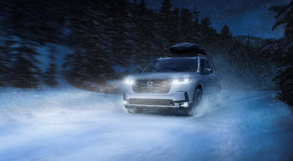 A new Honda Pilot for sale, a white 2024 Honda Pilot, is shown driving through the snow.