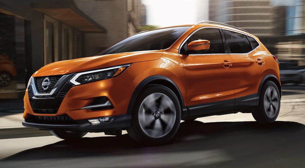 An orange 2022 Nissan Rogue Sport is shown driving on a city street after viewing a Nissan Rogue for sale.
