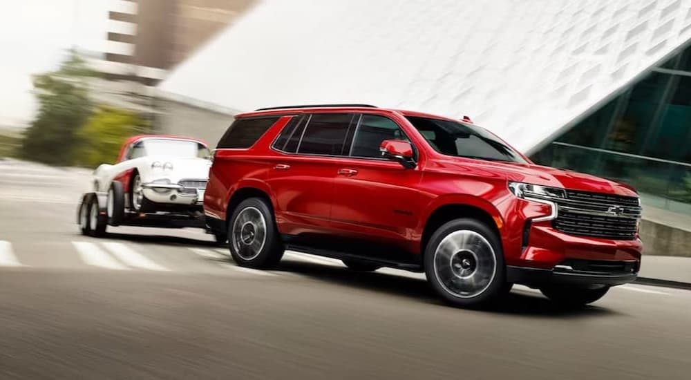 A red 2023 Chevy Tahoe is shown towing a car on a street.