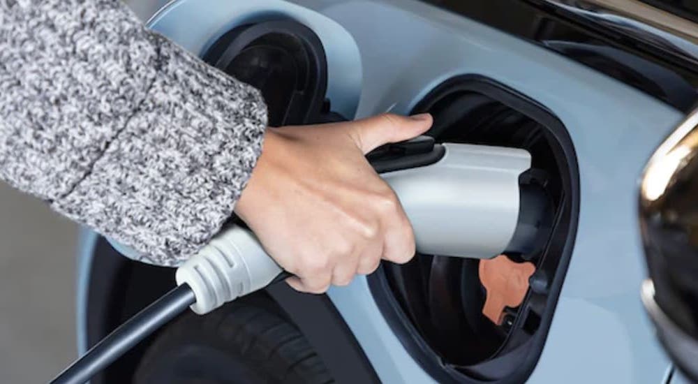 A person is shown charging a light blue 2023 Chevy Bolt EV.